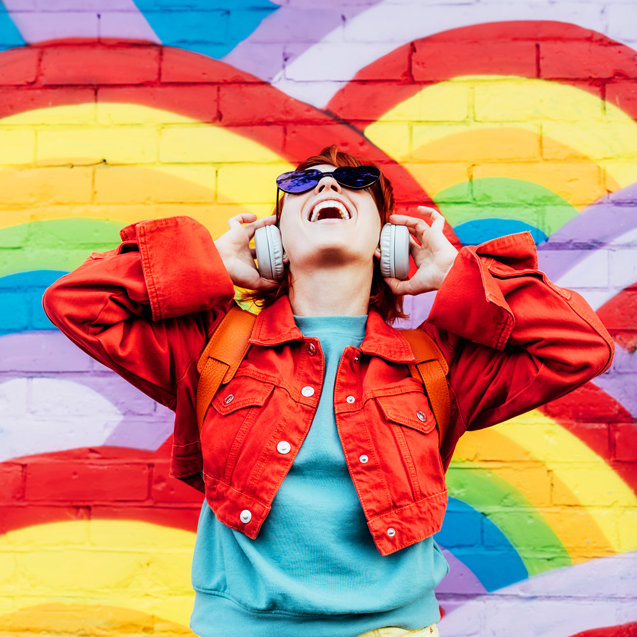 picture of an excited lady wearing headphones with a rainbow backdrop